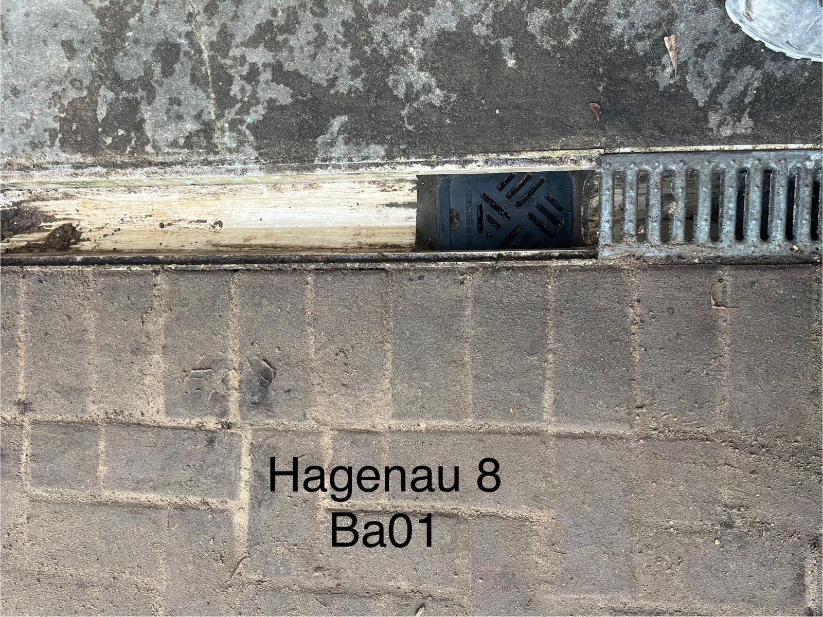 Odpływ liniowy z rusztem metalowym i elementem rewizyjnym Kessel wbudowany w nawierzchnię z kostki brukowej, widoczne zabrudzenia i wilgoć.