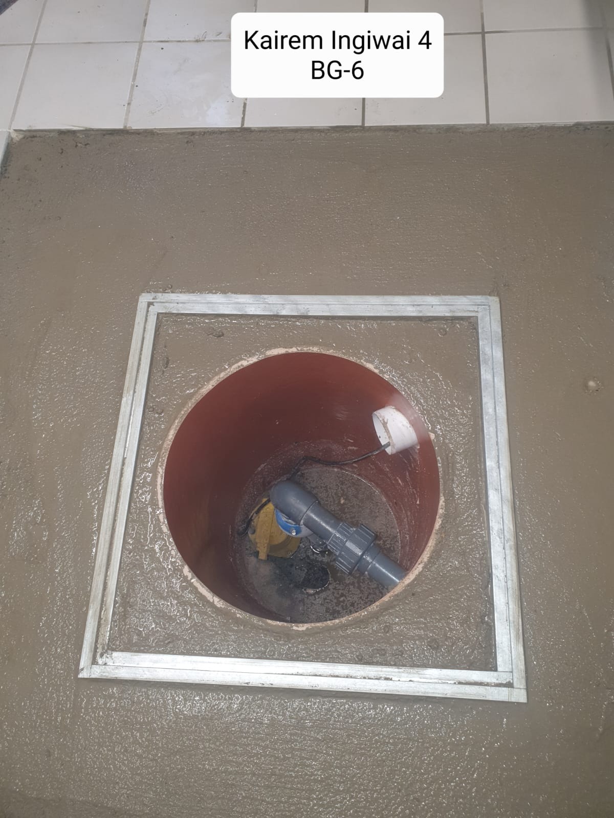 Świeżo wylany beton wokół okrągłego otworu z rurami i pompą w środku, zabezpieczonego metalową ramką.