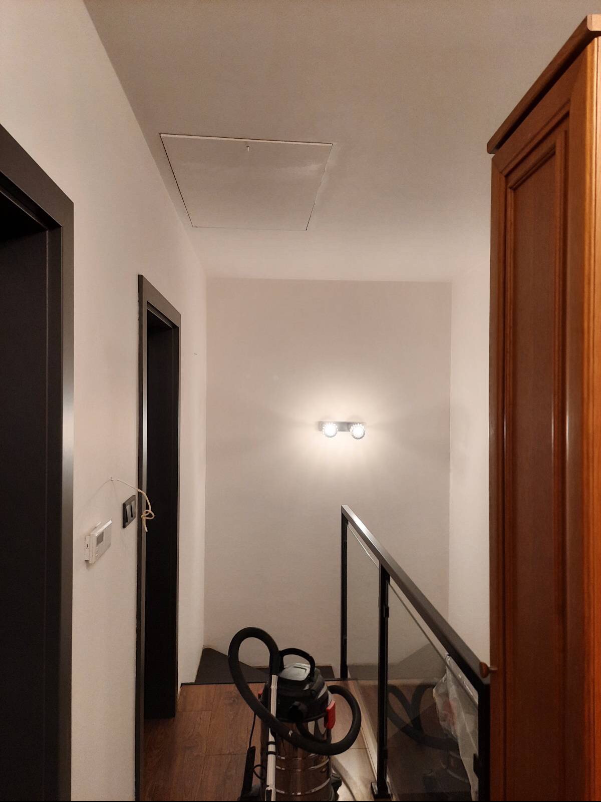 Korytarz w Tarczynie po szpachlowaniu, widoczny właz rewizyjny na suficie, lampa na ścianie, odkurzacz i fragment drewnianej szafy.