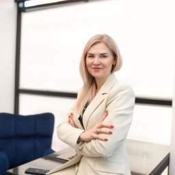 KANCELARIA BANKOWA KINGA BOYKE - Portret kobiety w jasnym garniturze, z założonymi rękami, siedzącej na biurku w biurze. W tle logo 'Kancelaria Bankowa' i niebieski fotel.