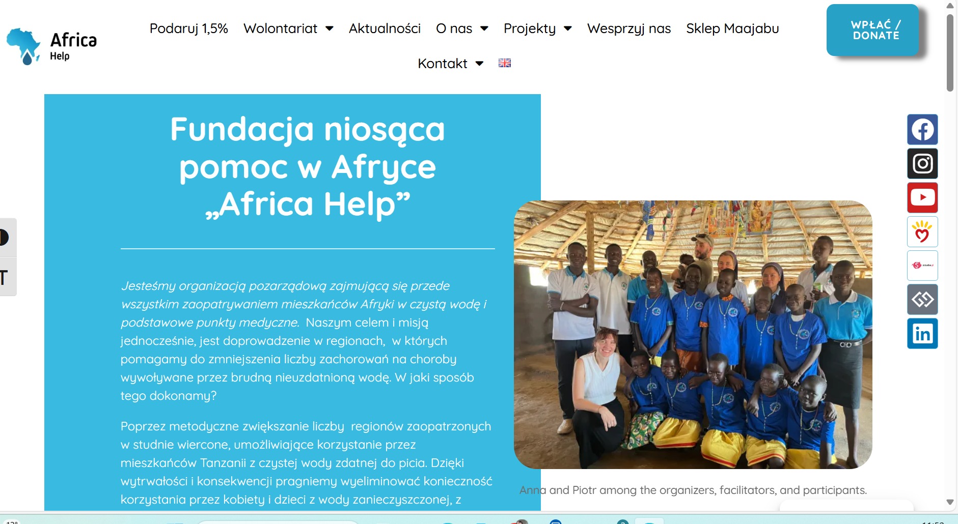 Zdjęcie grupowe dzieci i dorosłych w Afryce, wspieranych przez fundację, w tle tradycyjna afrykańska chata z dachem ze słomy, widoczne plakaty na ścianie.