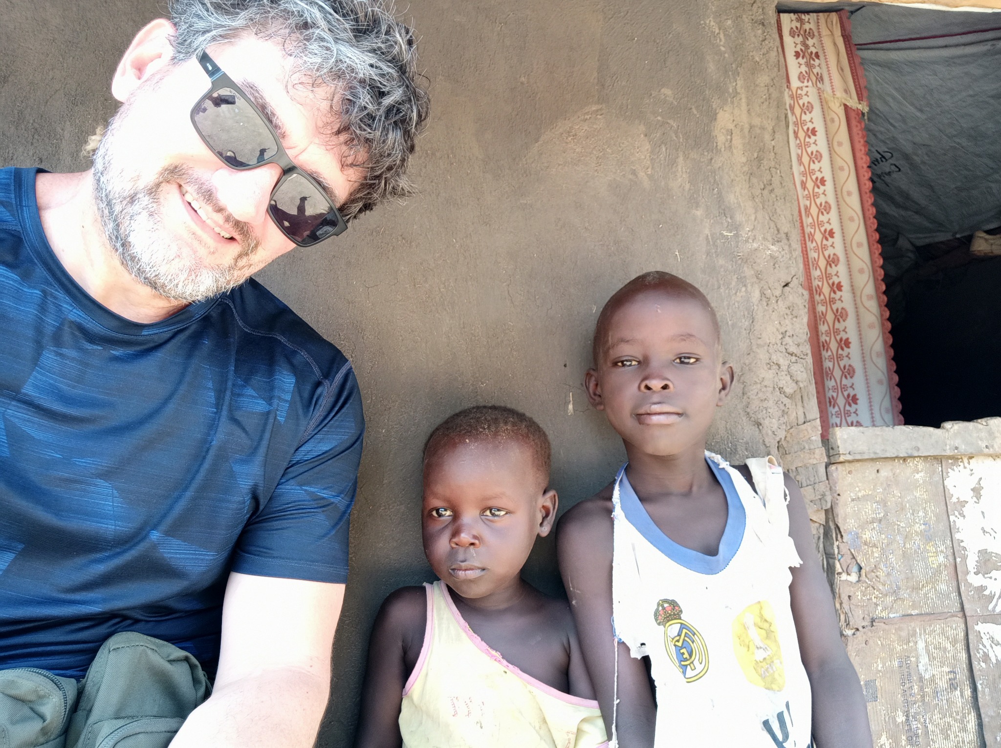 Zdjęcie zrobione w Poznaniu przedstawia uśmiechniętego mężczyznę w okularach przeciwsłonecznych, pozującego z dwójką dzieci na tle ściany i wejścia do namiotu.