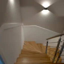 Drewniane schody spiralne z metalową balustradą, oświetlone dwoma nowoczesnymi lampami ściennymi, widok z góry.