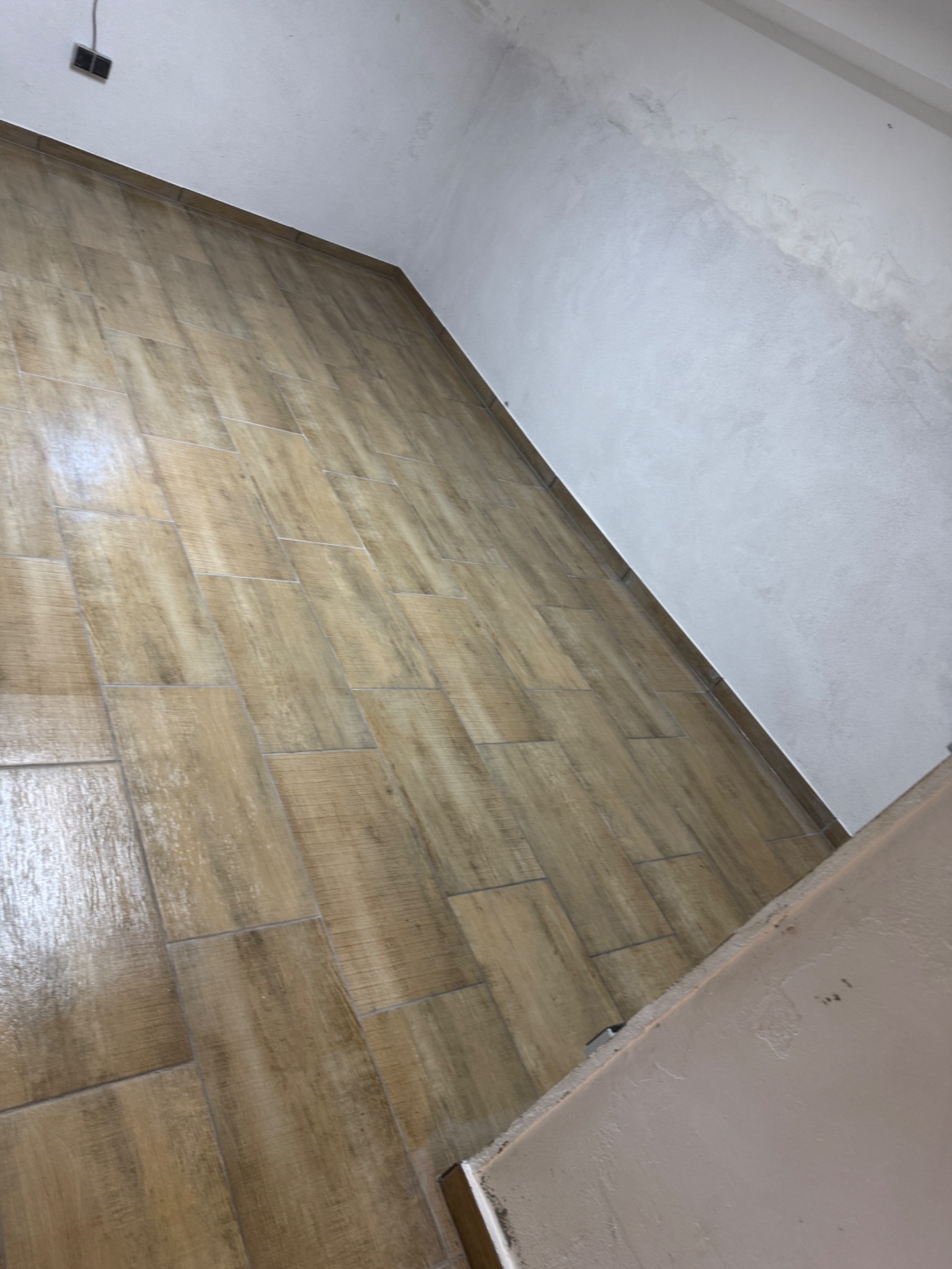 Ułożone płytki podłogowe imitujące drewno w nowym pomieszczeniu, widoczne surowe, pomalowane ściany.