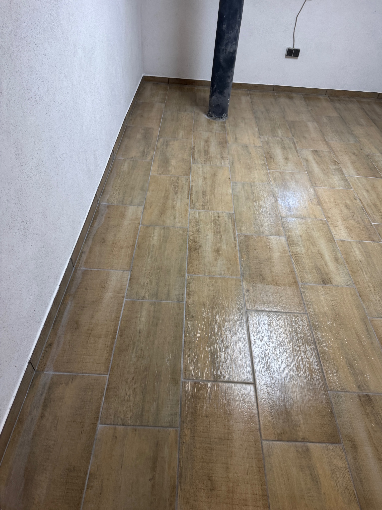 Ułożona podłoga z płytek imitujących drewno, widoczny pion kanalizacyjny i fragment ściany z gładzią, świeżo po fugowaniu.