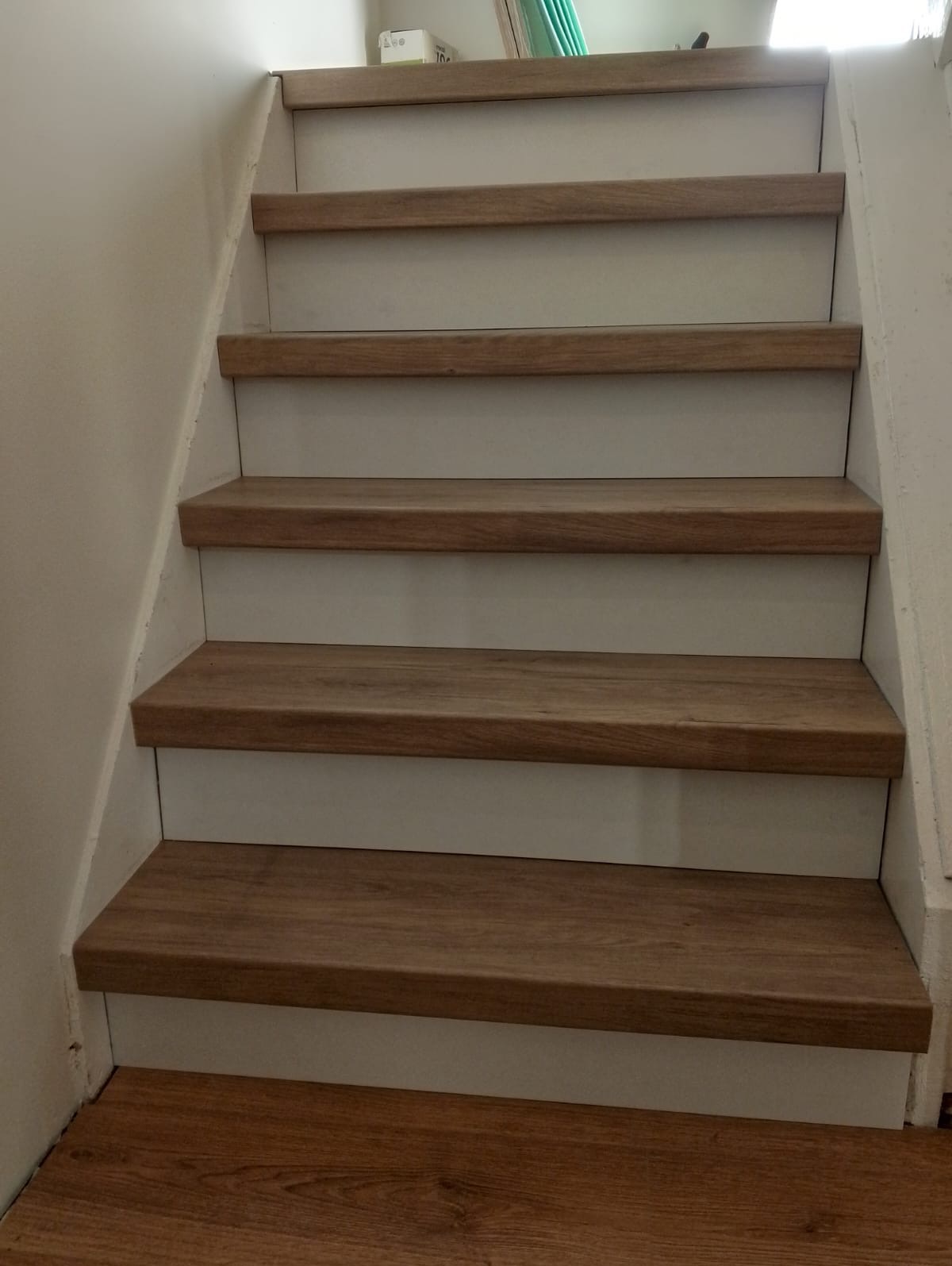 Schody wewnętrzne z drewnopodobnymi stopniami i białymi podstopnicami, widok z dołu.