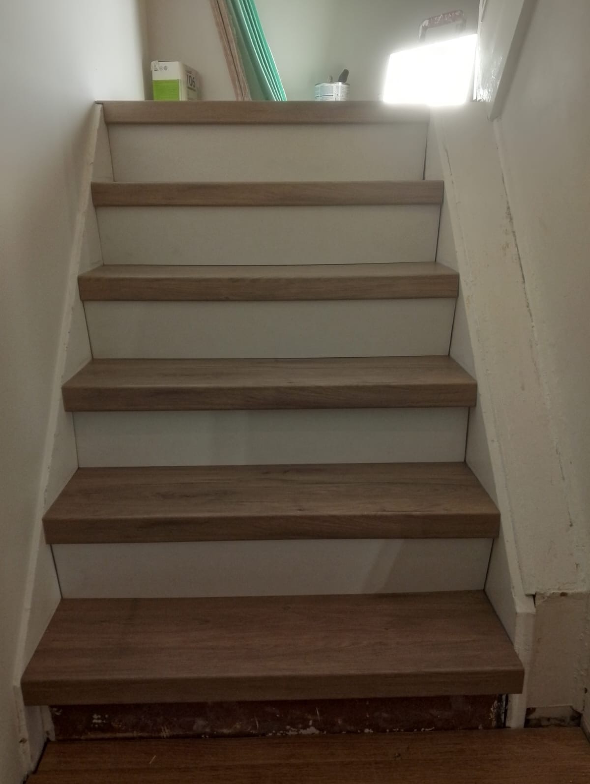 Schody wykończone panelami drewnopodobnymi, białe ściany, widoczne niedoskonałości wykończenia przy podłodze.