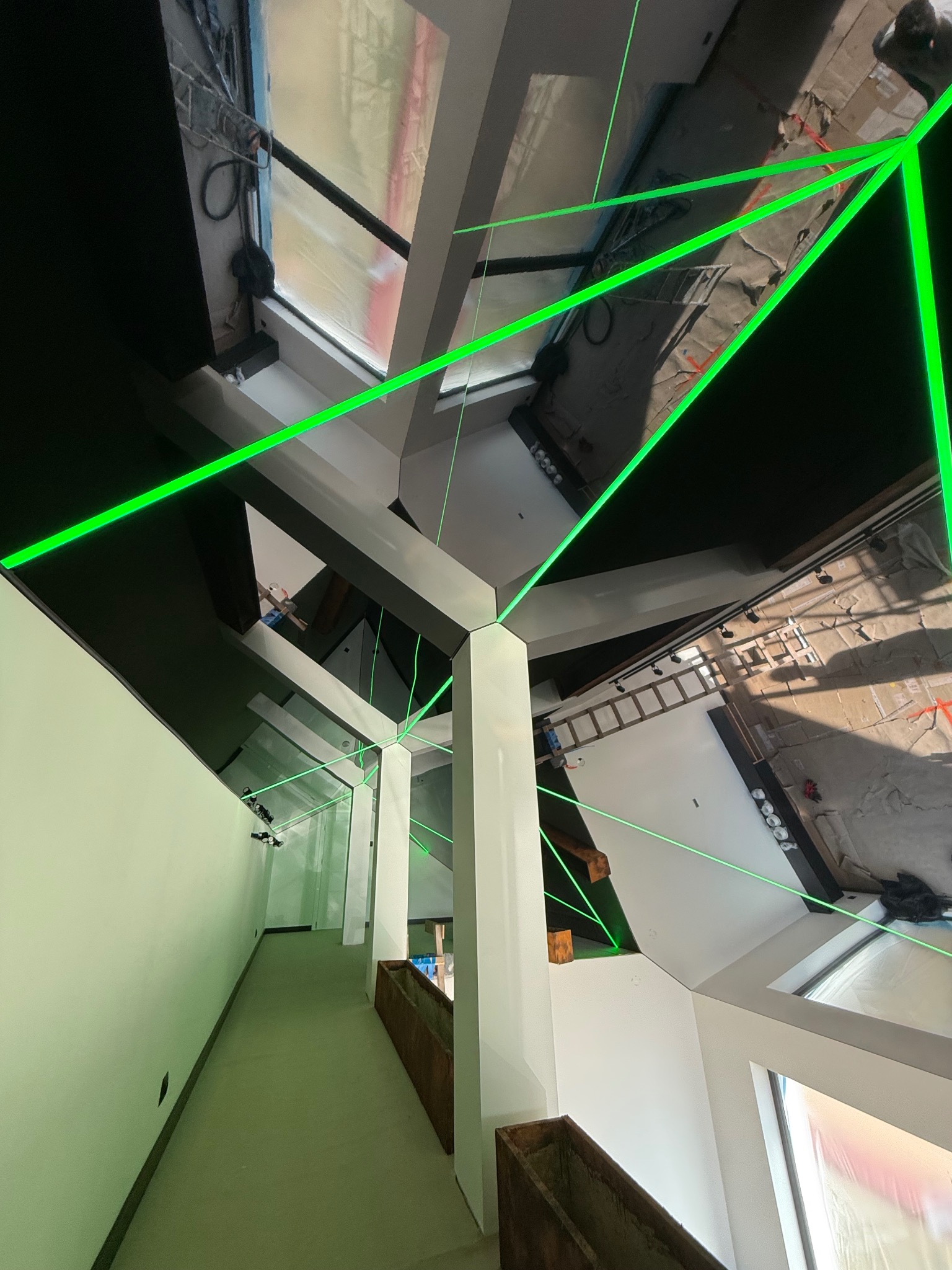 Montaż sufitu napinanego: widok z góry z zielonym laserem wyznaczającym poziom, widoczne elementy konstrukcyjne i przygotowane podłoże.