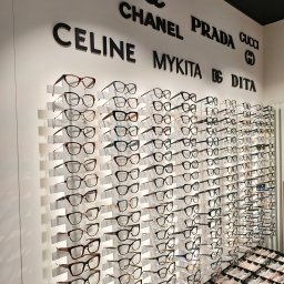 CENTRUM ZDROWIA OKA Michał Nowak - Ekspozycja oprawek okularów w salonie optycznym, marki takie jak Dior, Chanel, Prada, Celine, Mykita i Dita na ścianie, różnorodne modele w rzędach i w gablotach.