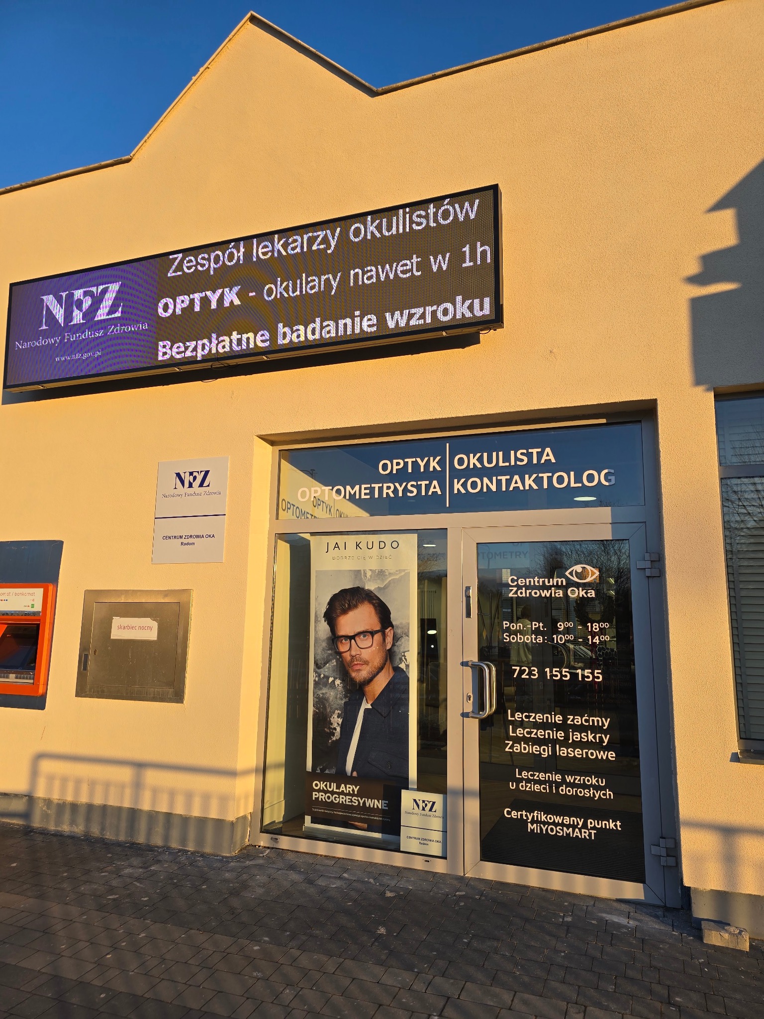 Fasada budynku Centrum Zdrowia Oka z szyldem informującym o zespole lekarzy okulistów, optyku oferującym okulary nawet w 1h oraz bezpłatnych badaniach wzroku, a także o leczeniu zaćmy, jaskry...