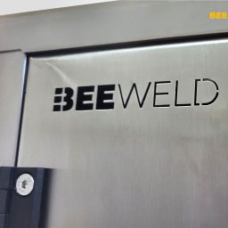 Bee Weld - Szczegółowe ujęcie metalowej konstrukcji z wyciętym laserowo napisem 'BEEWELD', z widocznymi elementami mocującymi. Precyzyjne wykonanie.