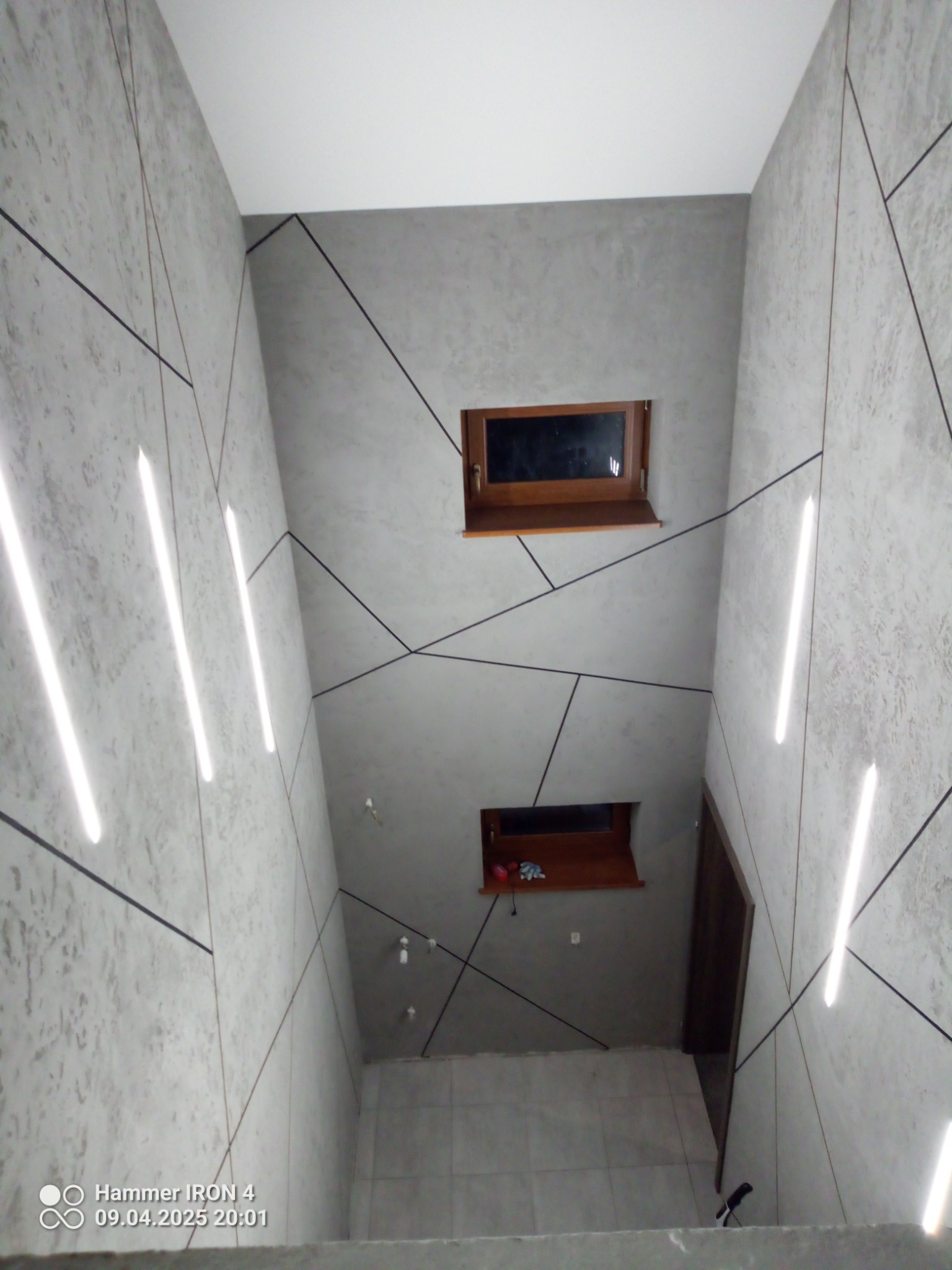 Nowoczesne wykończenie klatki schodowej: szare ściany z geometrycznym wzorem, podświetlane listwy LED i drewniane okna w ścianie. Widok z góry.