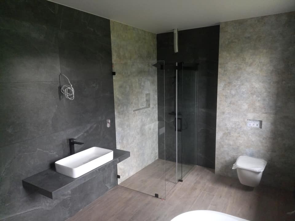 Nowoczesna łazienka z kabiną prysznicową typu walk-in, umywalką nablatową na kamiennym blacie i szarą płytką imitującą kamień na ścianach. Minimalistyczny design.