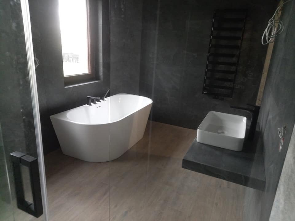 Nowoczesna łazienka z wolnostojącą wanną, umywalką nablatową i grzejnikiem drabinkowym na tle ciemnych płytek. Minimalistyczny design z akcentami czerni.