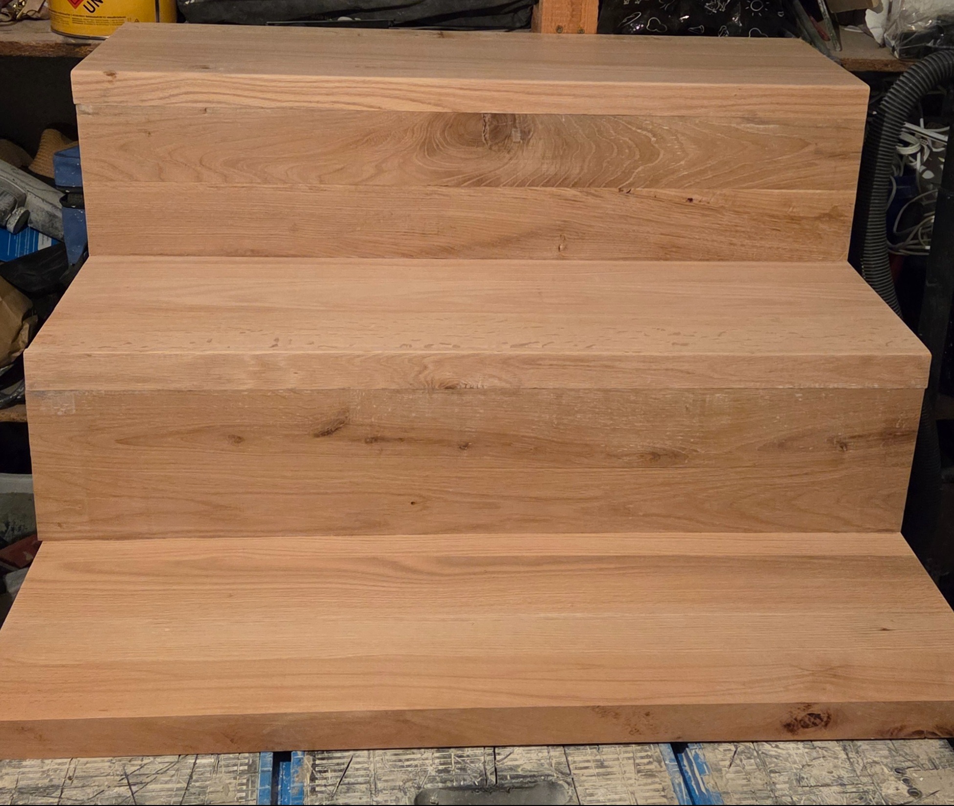 Trzy stopnie schodów z jasnego drewna dębowego, widoczne z bliska, ukazujące naturalne usłojenie i ciepłą barwę materiału. Stopnie ułożone na roboczym stole.