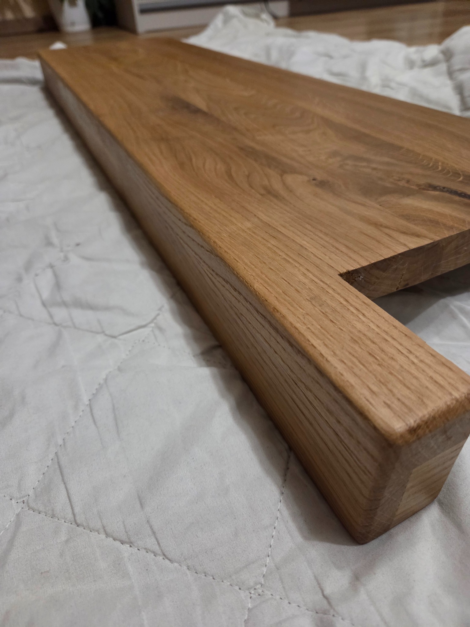 Fragment blatu drewnianego z widocznym usłojeniem, leżącego na białej tkaninie. Ujęcie z bliska podkreśla detale wykończenia i naturalny charakter drewna.
