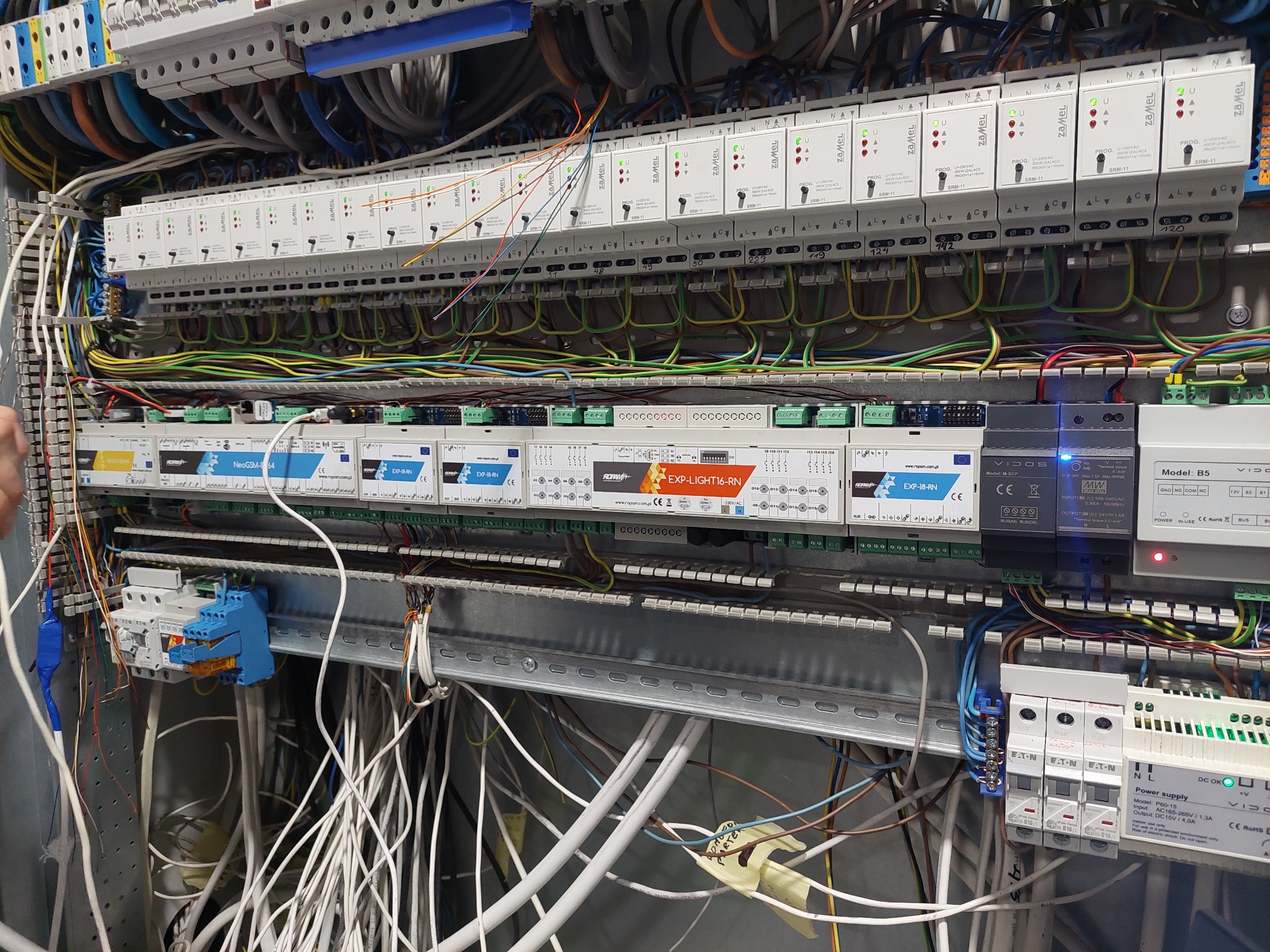 Rozbudowana szafa rozdzielcza z licznymi modułami, przewodami i zabezpieczeniami, widok z bliska na skomplikowaną instalację elektryczną w obudowie metalowej.