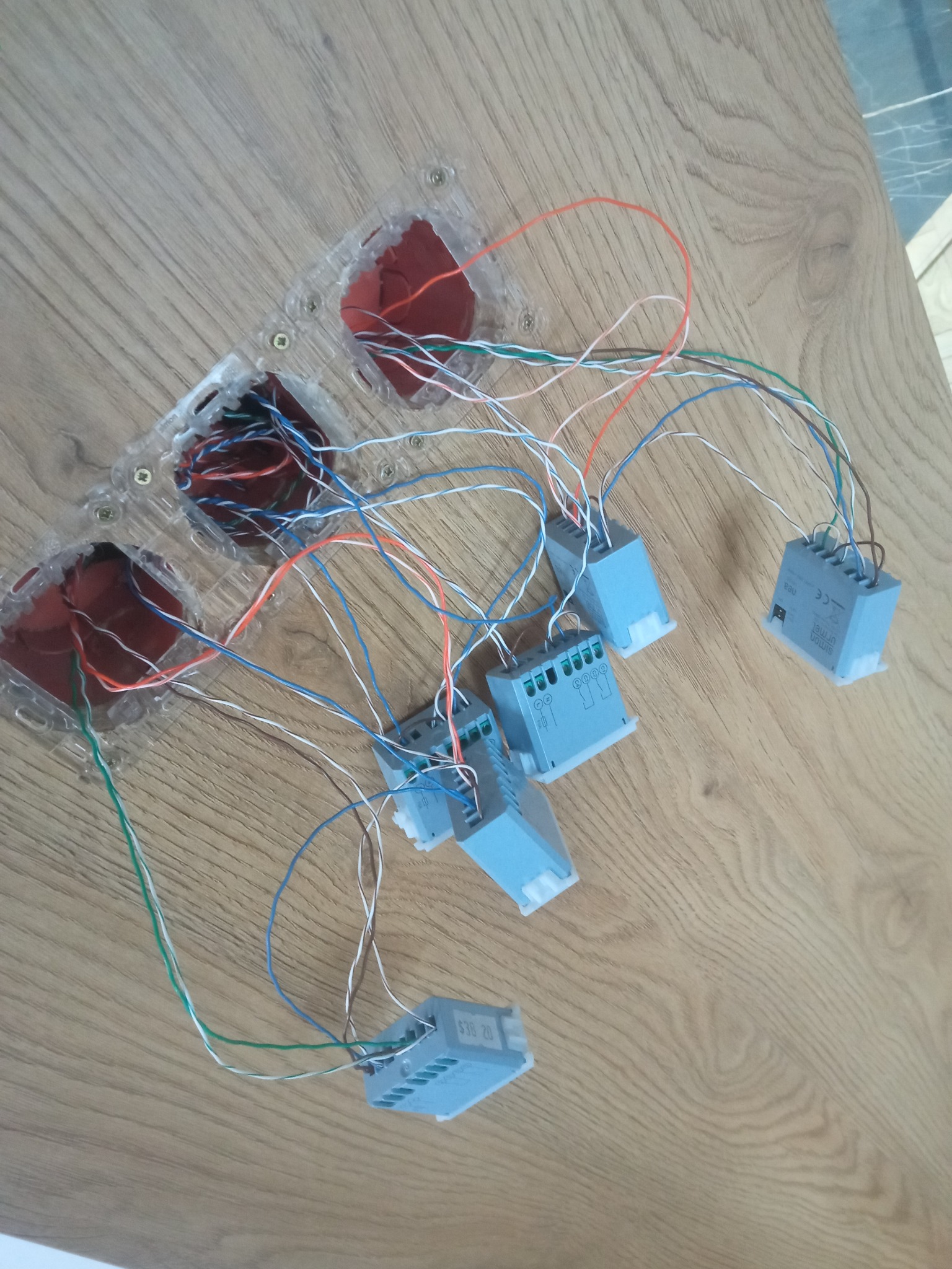 Przygotowanie do montażu instalacji elektrycznej: kable prowadzone z puszek podtynkowych do modułów sterujących na drewnianym blacie.