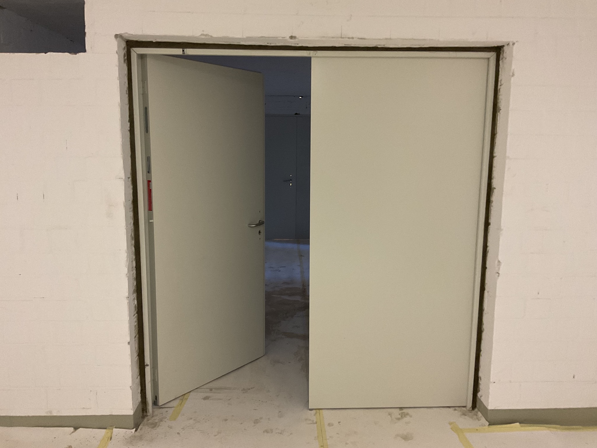 Montaż dwuskrzydłowych drzwi wewnętrznych w surowym otworze, widoczne detale mocowania i szczelina między skrzydłami. Otwarta lewa strona drzwi.