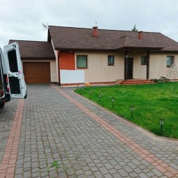 GrzesiekMaluje - Dom jednorodzinny w trakcie prac elewacyjnych: fragment pomalowanej ściany, zabezpieczone okno, drabina i otwarty samochód dostawczy z narzędziami.