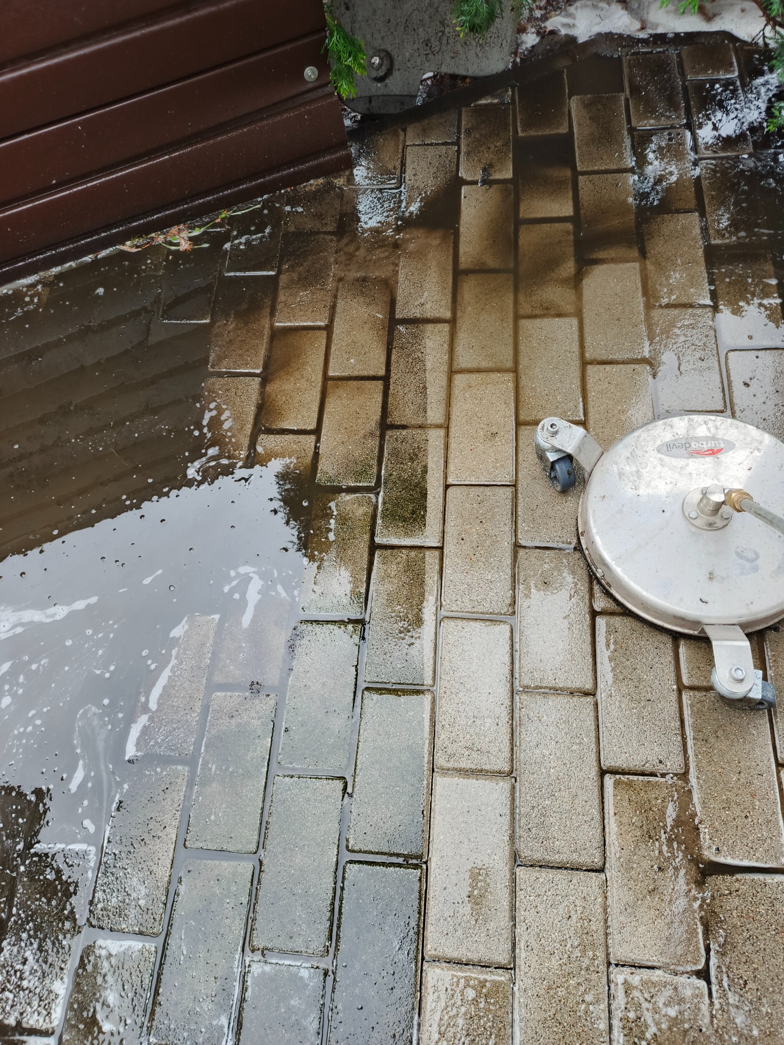 Mycie kostki brukowej urządzenia wysokociśnieniowego. Widoczna różnica między czystą a brudną powierzchnią. Częściowo zalana wodą.