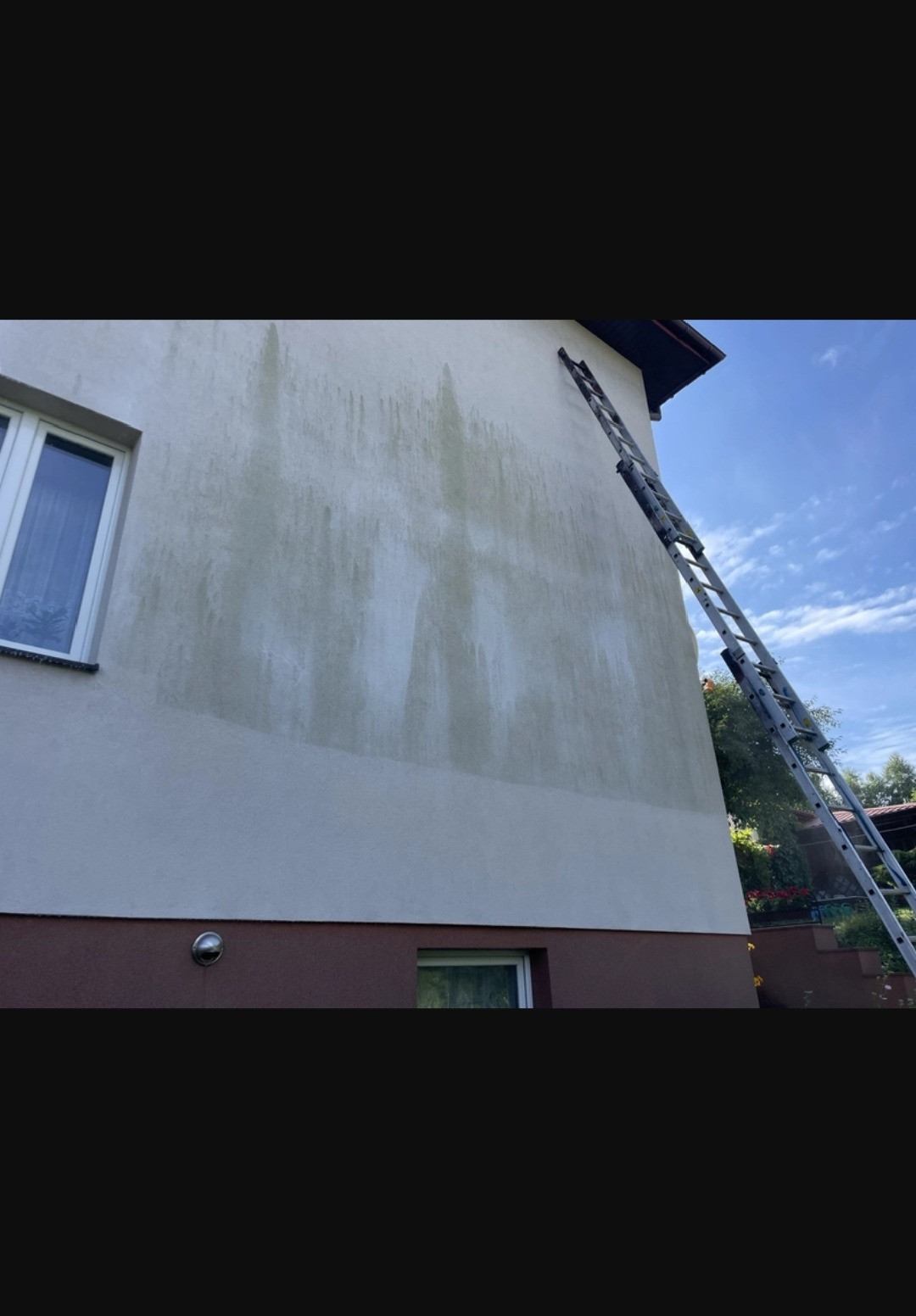 Fragment elewacji budynku z widocznymi śladami czyszczenia, z drabiną opartą o ścianę. Częściowo umyta elewacja kontrastuje z zabrudzoną powierzchnią.
