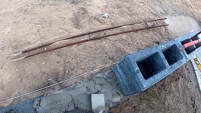 Wyrównywanie betonowych bloczków fundamentowych zaprawą, widoczne pręty zbrojeniowe i poziomica.