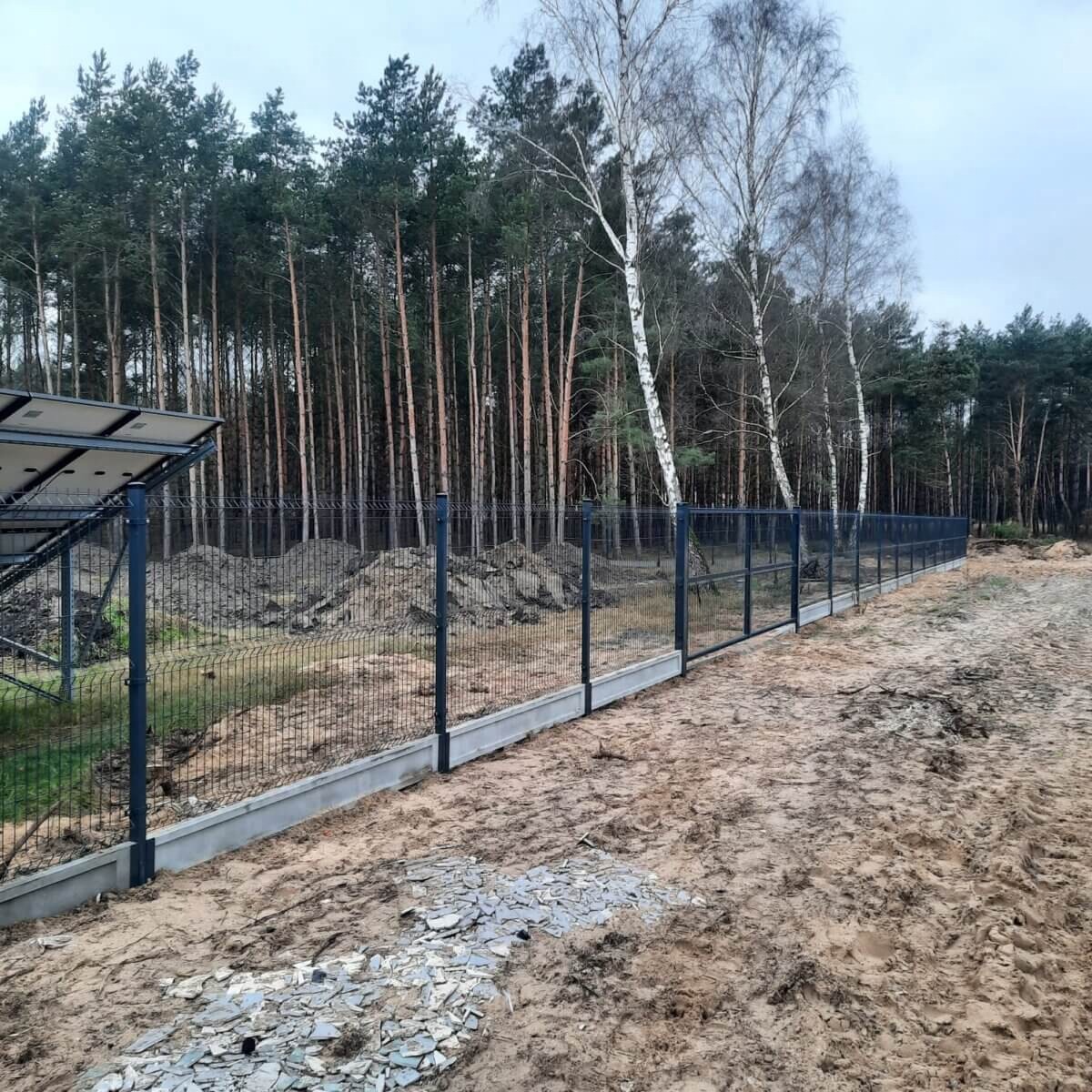 Ogrodzenie panelowe z podmurówką betonową w Koronowie, widoczne panele fotowoltaiczne w tle.