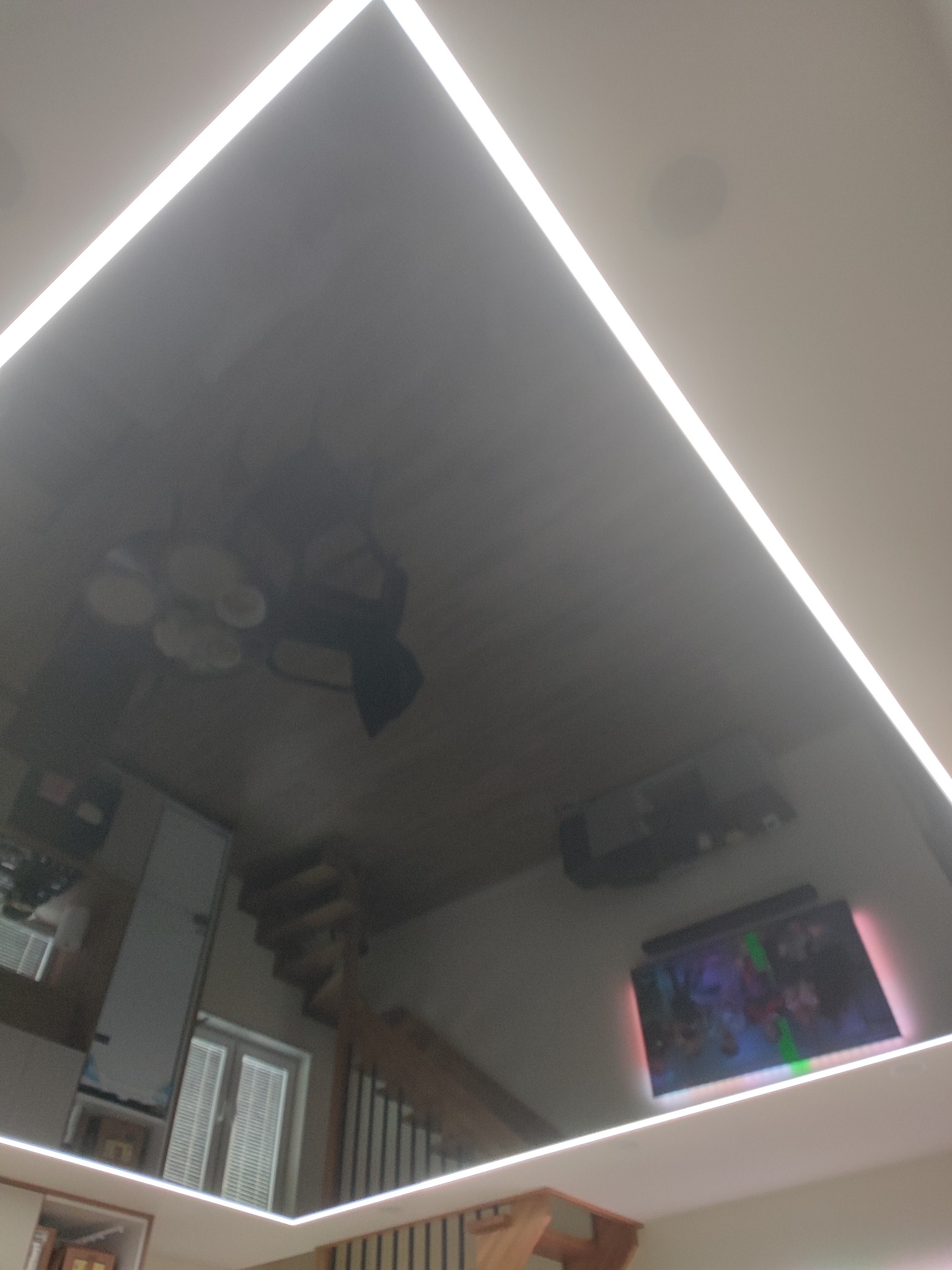 Błyszczący, czarny sufit z odblaskami wnętrza, obramowany listwami LED, tworzący iluzję głębi i nowoczesny design.