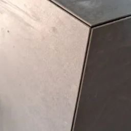 Precyzyjnie ułożone, szare płytki ceramiczne na rogu ściany, z widocznymi narzędziami glazurniczymi w tle. Detal wykończenia, wąska spoina, ostre krawędzie.