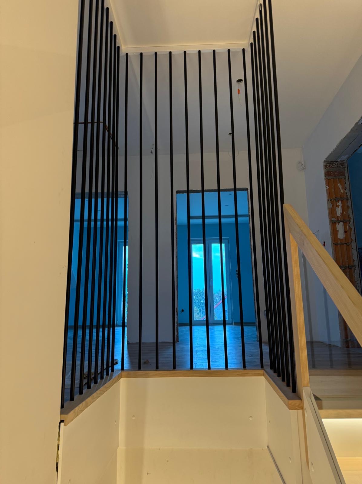 Nowoczesna balustrada schodowa z czarnych, pionowych prętów, widok z dołu schodów na otwarte przestrzenie w surowym stanie.