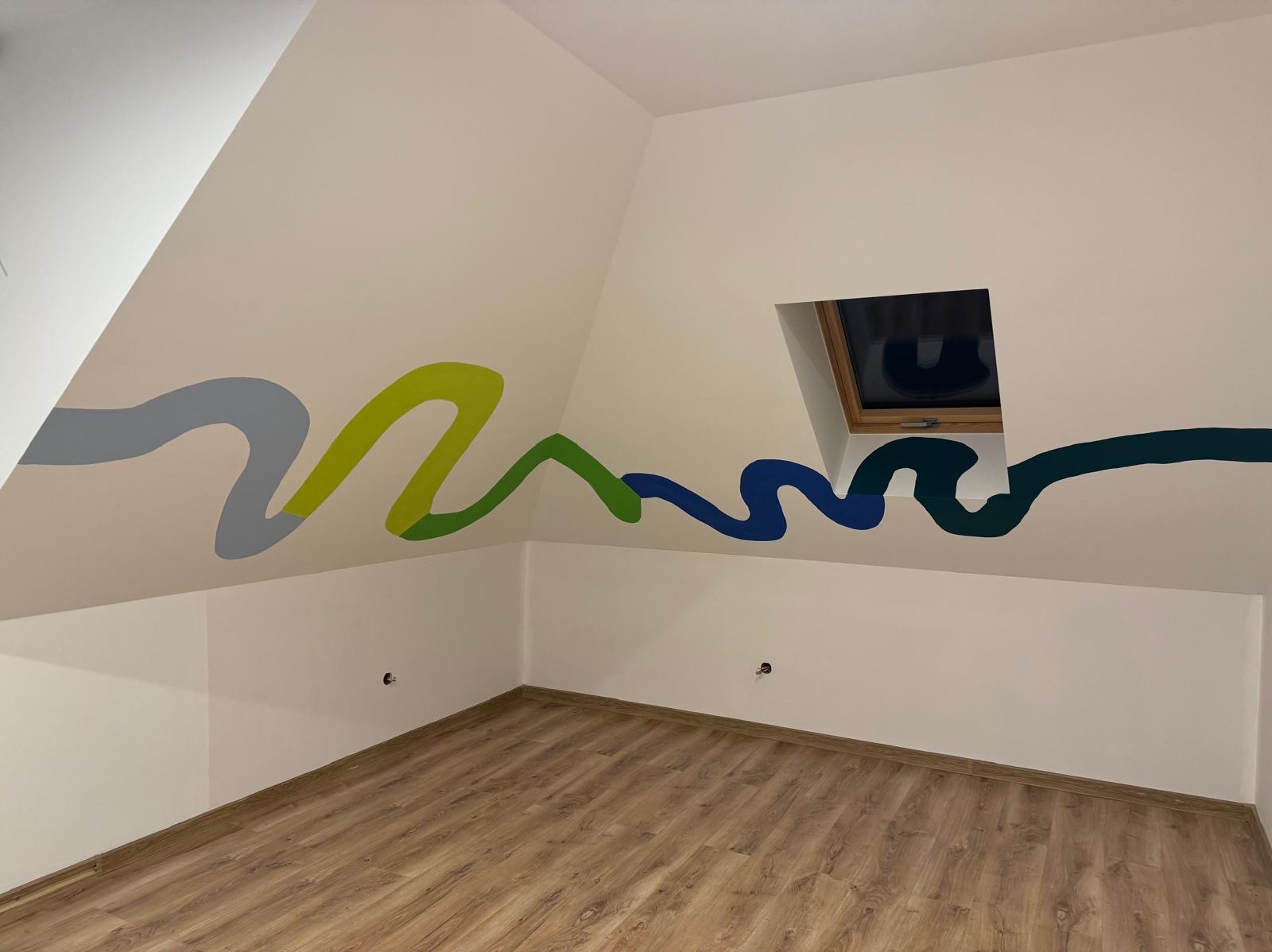 Pomalowane ściany poddasza z oknem dachowym w kolorowe, faliste wzory; podłoga wyłożona panelami imitującymi drewno.