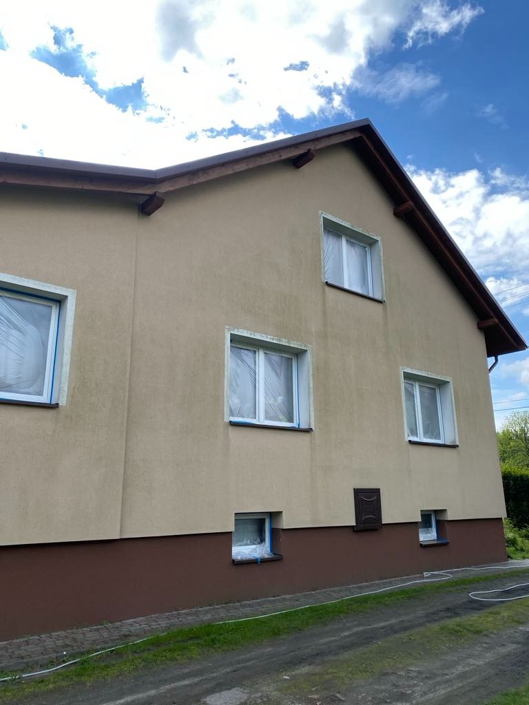 Elewacja domu przed malowaniem: okna zabezpieczone folią, widoczne zabrudzenia na ścianach. Przygotowanie do prac malarskich na zewnątrz budynku.