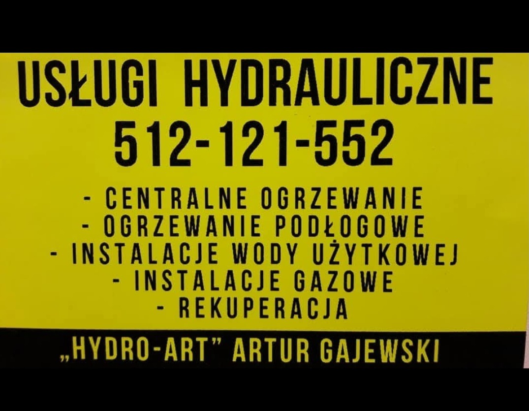 Żółta tablica reklamowa z czarnym tekstem oferująca usługi hydrauliczne, w tym centralne ogrzewanie, ogrzewanie podłogowe, instalacje wody użytkowej, instalacje gazowe i rekuperację, z numerem...
