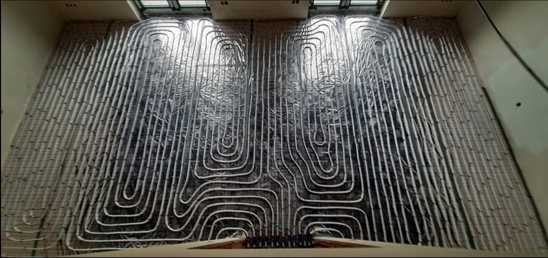 Układanie rur ogrzewania podłogowego na folii izolacyjnej, widok z góry na rozłożony system przed zalaniem wylewką.