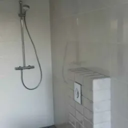 Nowoczesna łazienka z podwieszaną toaletą, szarymi płytkami i minimalistyczną armaturą prysznicową.