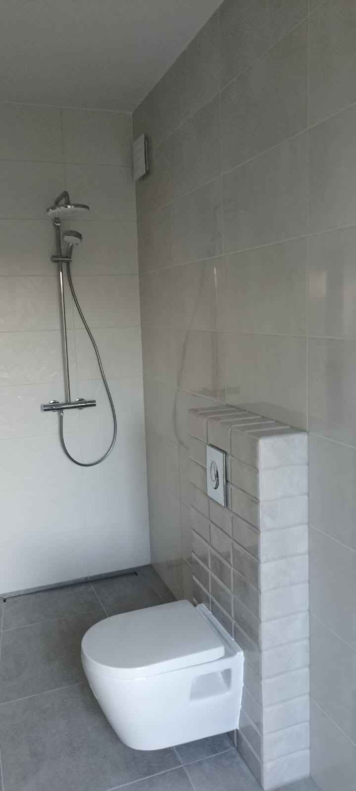 Nowoczesna łazienka z podwieszaną toaletą, szarymi płytkami i minimalistyczną armaturą prysznicową.