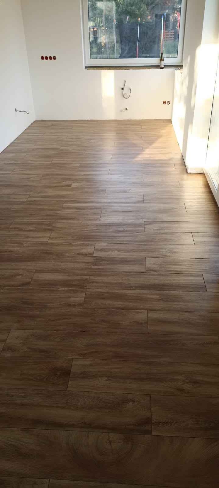 Ułożona podłoga z paneli imitujących drewno w nowym pomieszczeniu, widoczne gniazdka elektryczne i okno z widokiem na zewnątrz.