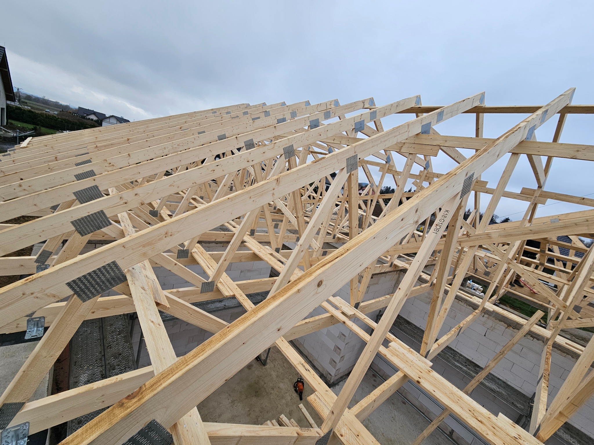 Drewniana konstrukcja więźby dachowej z metalowymi łącznikami, widok z góry na budynek w trakcie budowy.