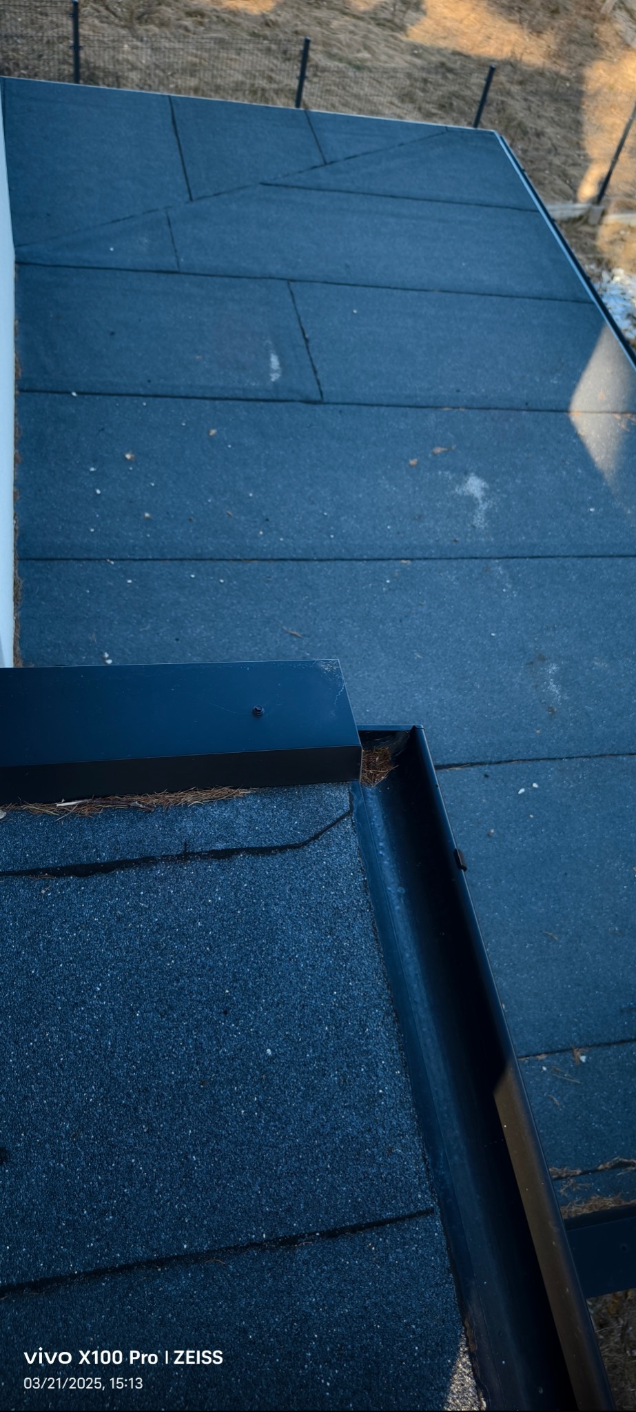 Fragment dachu pokrytego papą z widoczną czarną rynną i obróbką blacharską, widok z góry, lekki cień.