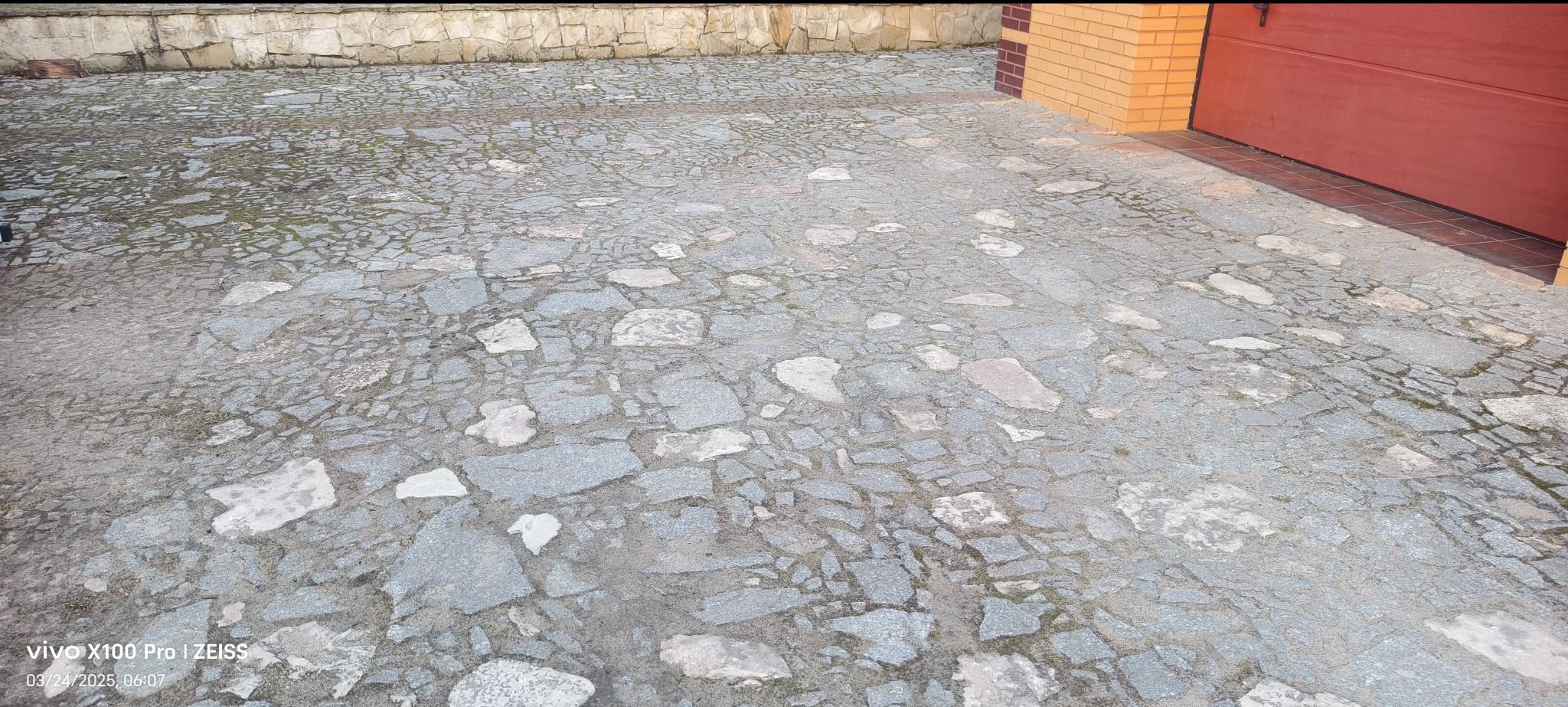 Szara kostka brukowa ułożona przed garażem w Gdańsku, widoczne nieregularne kształty kamieni i fugi wypełnione piaskiem.