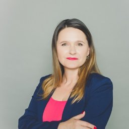 Studio Kreacji - Portret kobiety w granatowej marynarce na szarym tle w Warszawie. Uśmiechnięta, z rękami skrzyżowanymi. Profesjonalny wizerunek grafika.