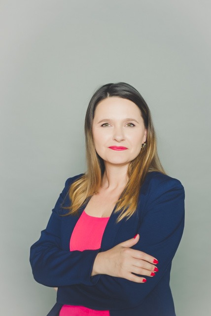 Portret kobiety w granatowej marynarce na szarym tle w Warszawie. Uśmiechnięta, z rękami skrzyżowanymi. Profesjonalny wizerunek grafika.