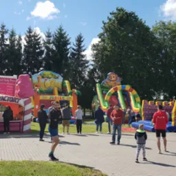 Kolorowe dmuchańce: zamek, dżungla, Candy Factory. Ludzie w tle. Słoneczny dzień, impreza plenerowa.