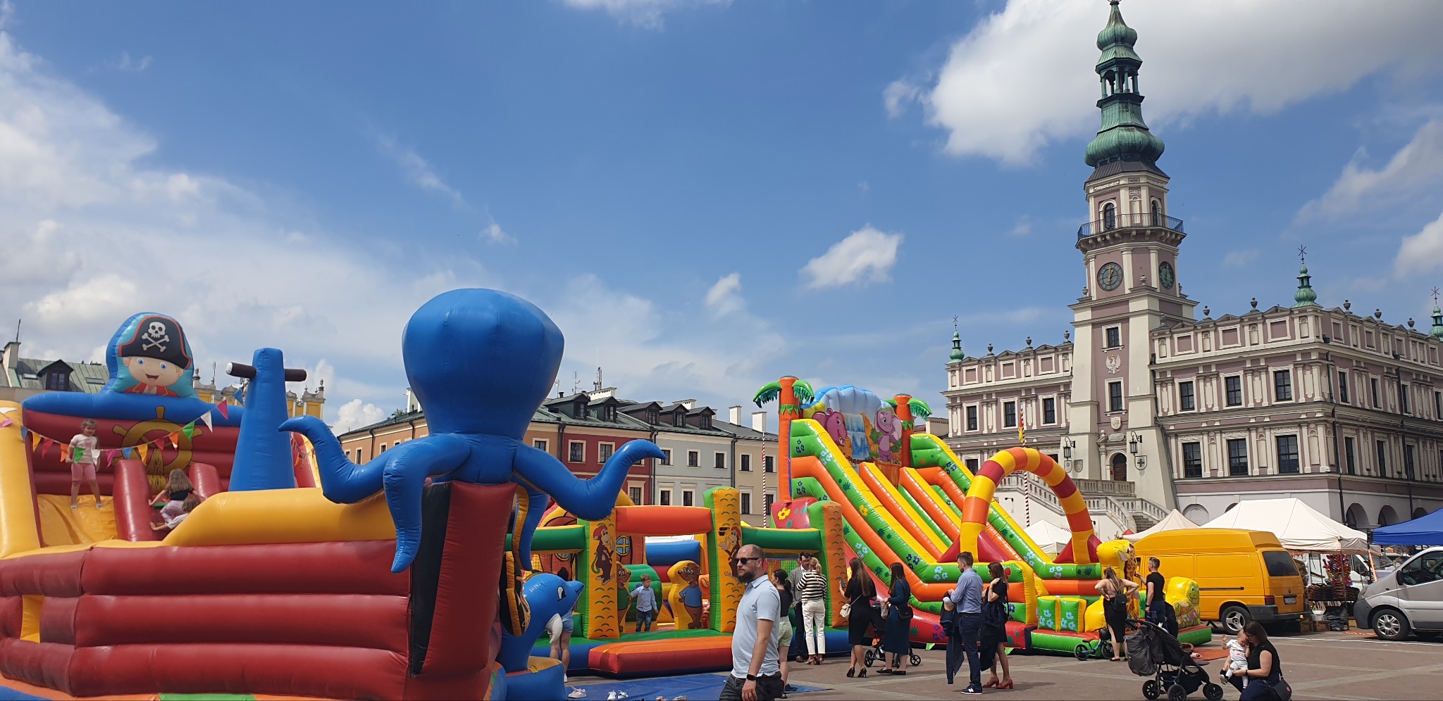 Kolorowe dmuchańce z motywami pirackimi i morskimi, ustawione na placu miejskim z zabytkową architekturą w tle, dzieci bawiące się na konstrukcji.