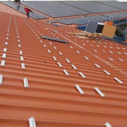 TRANSMAR MARCIN KĘPSKI - Montaż paneli na dachu z blachy trapezowej, widoczne szyny montażowe, pracownicy na dachu instalują panele w pochmurny dzień.