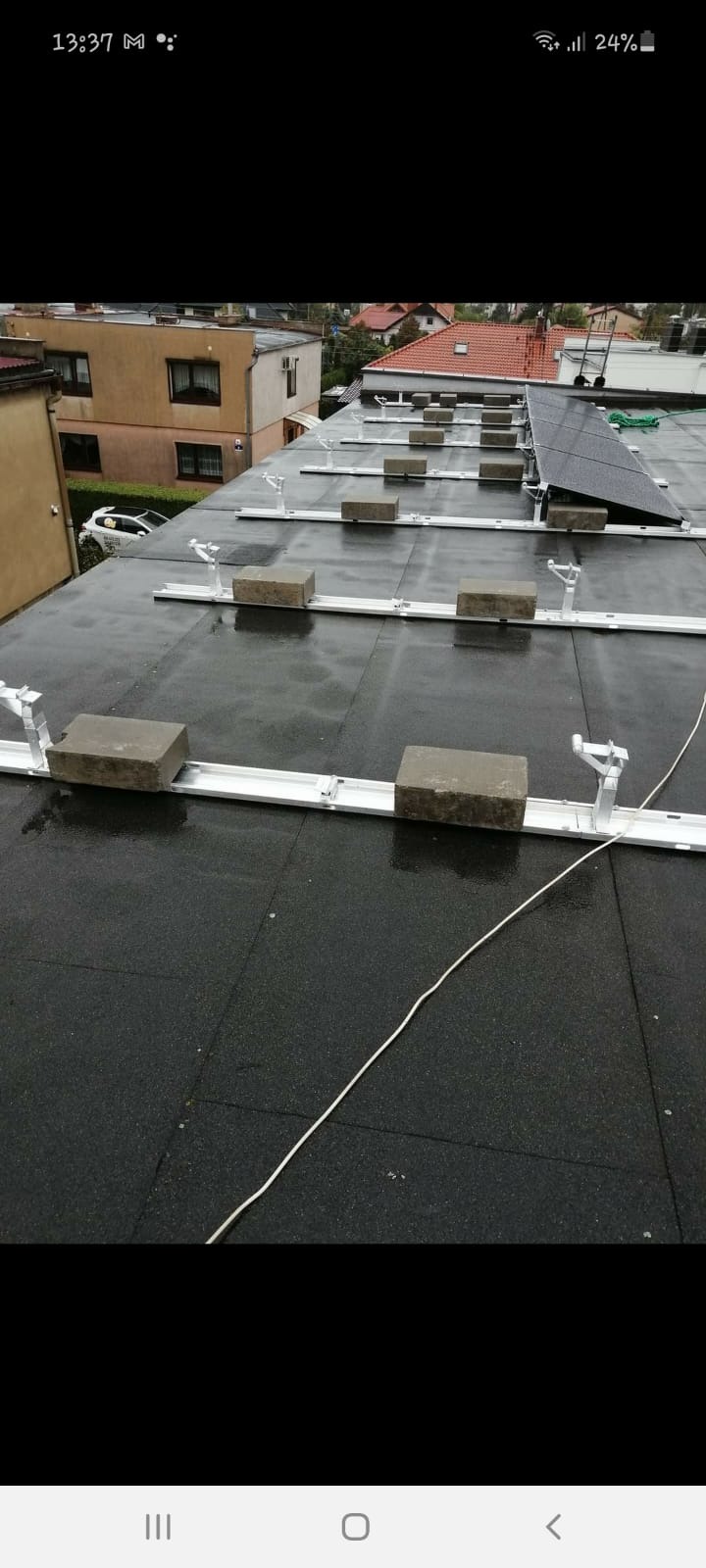 Montaż konstrukcji wsporczej pod panele fotowoltaiczne na płaskim dachu, z widocznymi betonowymi obciążnikami i częściowo zamontowanym panelem.