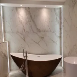 Nowoczesna łazienka z wolnostojącą, brązową wanną i marmurowymi płytkami ściennymi z subtelnym oświetleniem LED wzdłuż krawędzi.