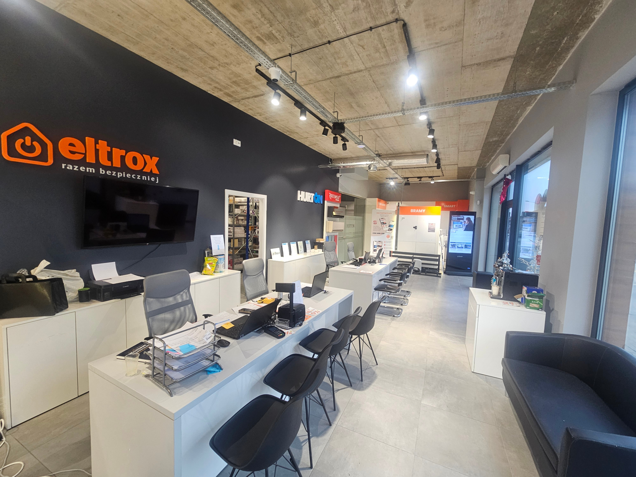 Wnętrze biura firmy Eltrox, specjalizującej się w systemach alarmowych i instalacjach elektrycznych, z widocznym logo na ścianie, stanowiskami obsługi klienta i ekspozycją produktów.