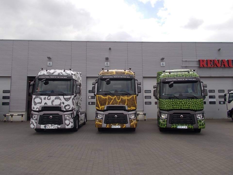 Trzy ciężarówki Renault z nadrukami imitującymi skórę zwierząt (leopard, żyrafa, krokodyl) stojące przed budynkiem z bramami garażowymi.
